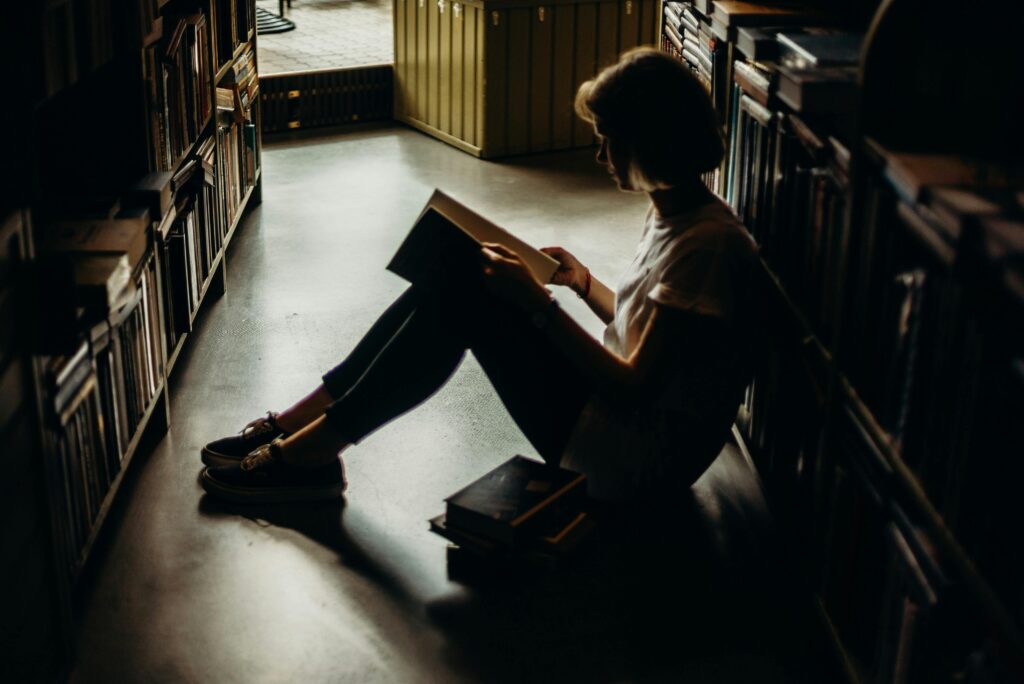 pexels-photo-2925308-2925308 A young woman engrossed in a book, sitting on the floor of a quiet library, creating a cozy reading atmosphere.