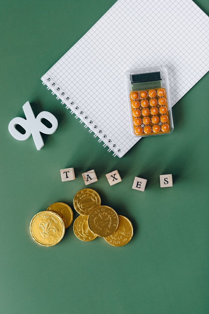 about-us-01 Flat lay of calculator, gold coins, notebook, and tax symbols on a green background.